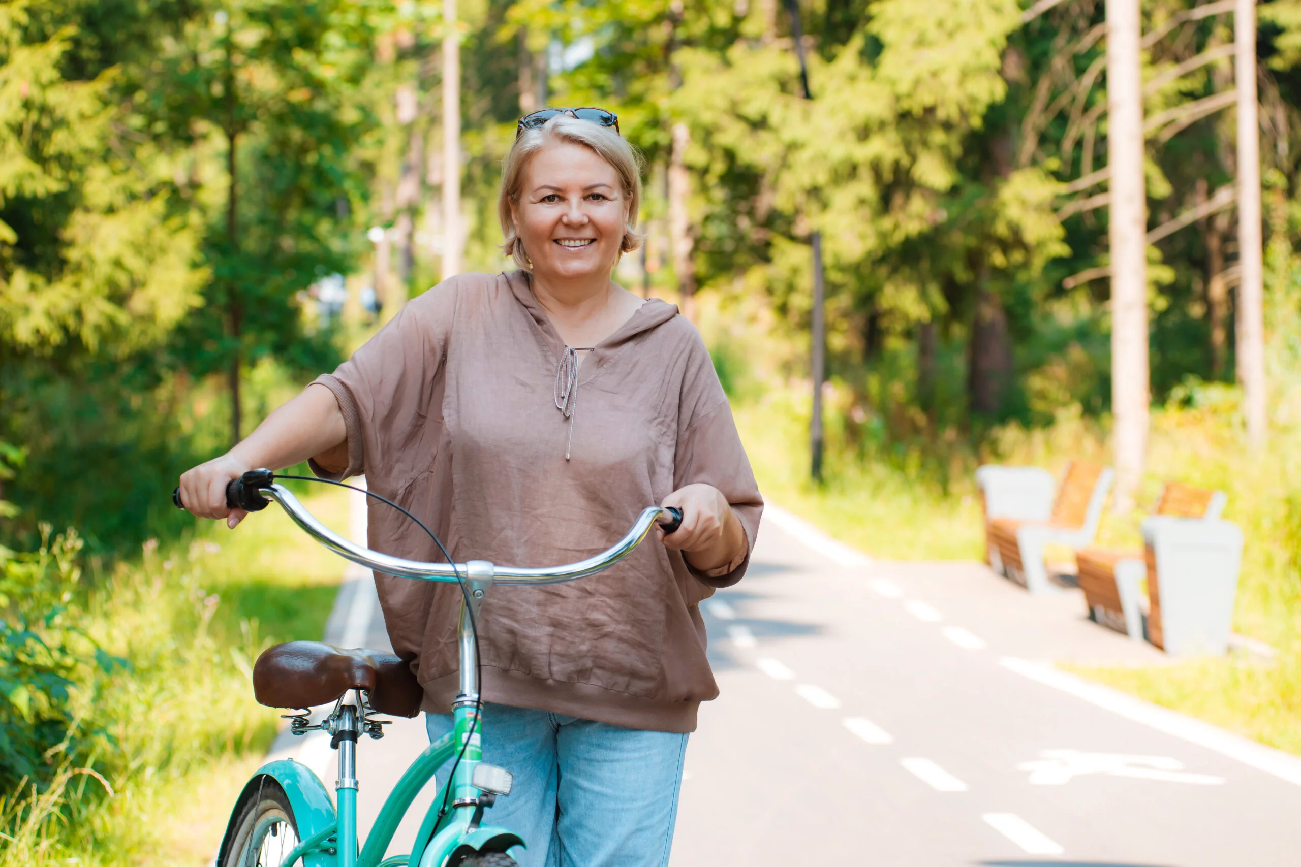 Senior older elderly modern woman rides a bicycle in a city park in the forest. Active pensioner, health lifestyle